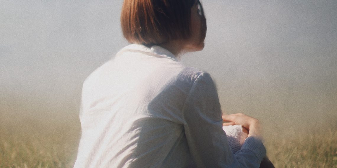 woman in white long sleeve shirt sitting on green grass field during daytime